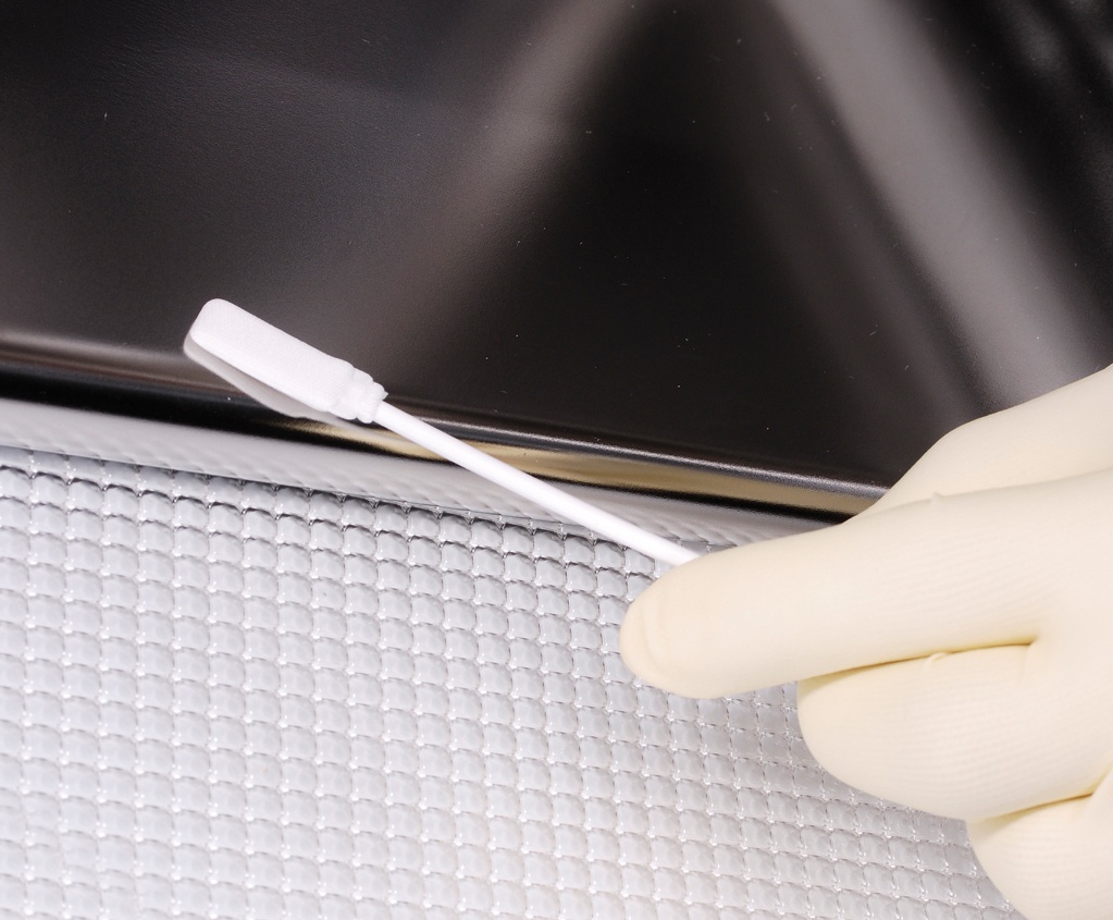 close up of white gloves holding cotton swab on metal surface
