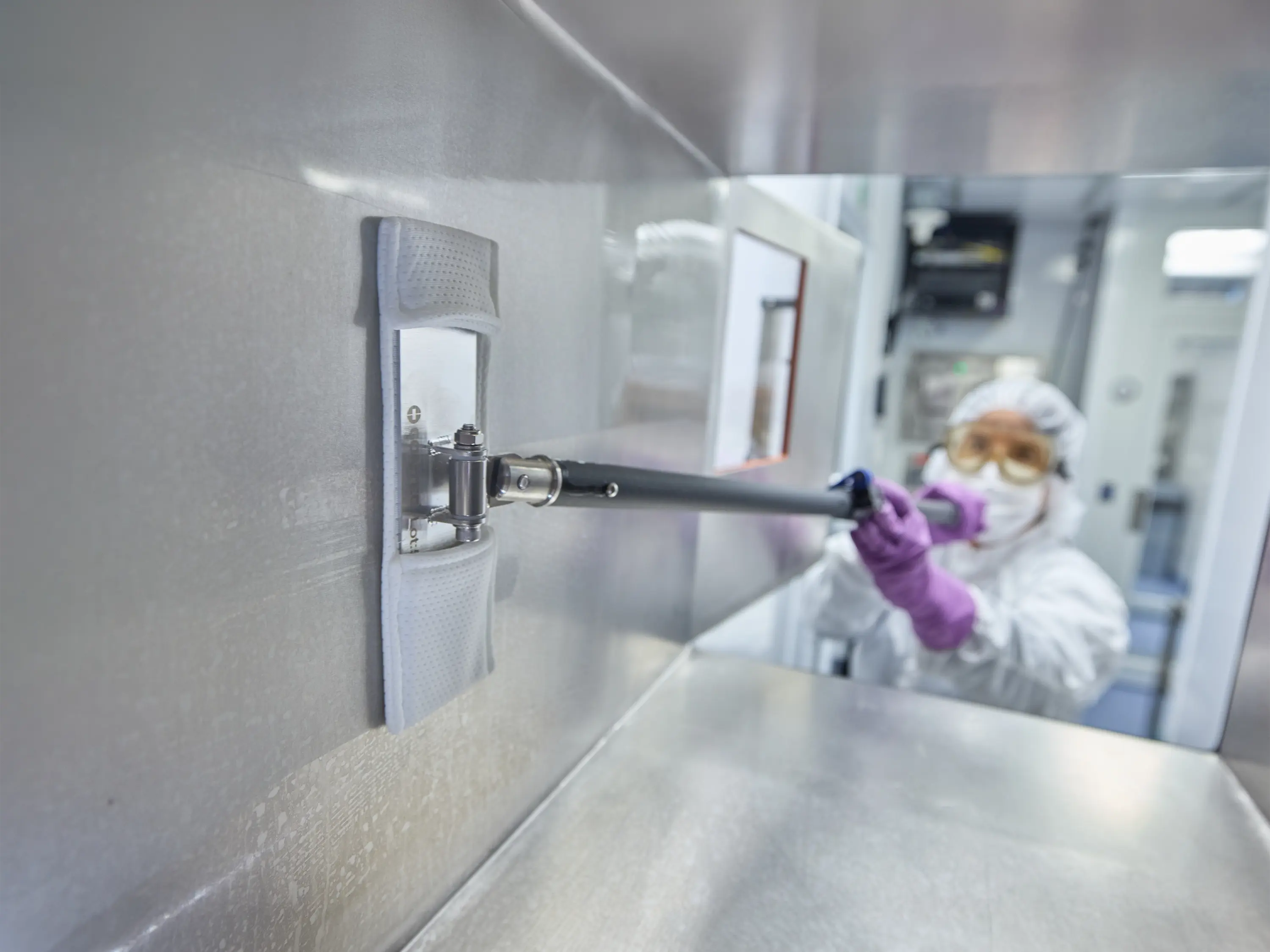 Cleanroom operator using an EasyReach cleaning tool to clean the interior wall of a passthrough.