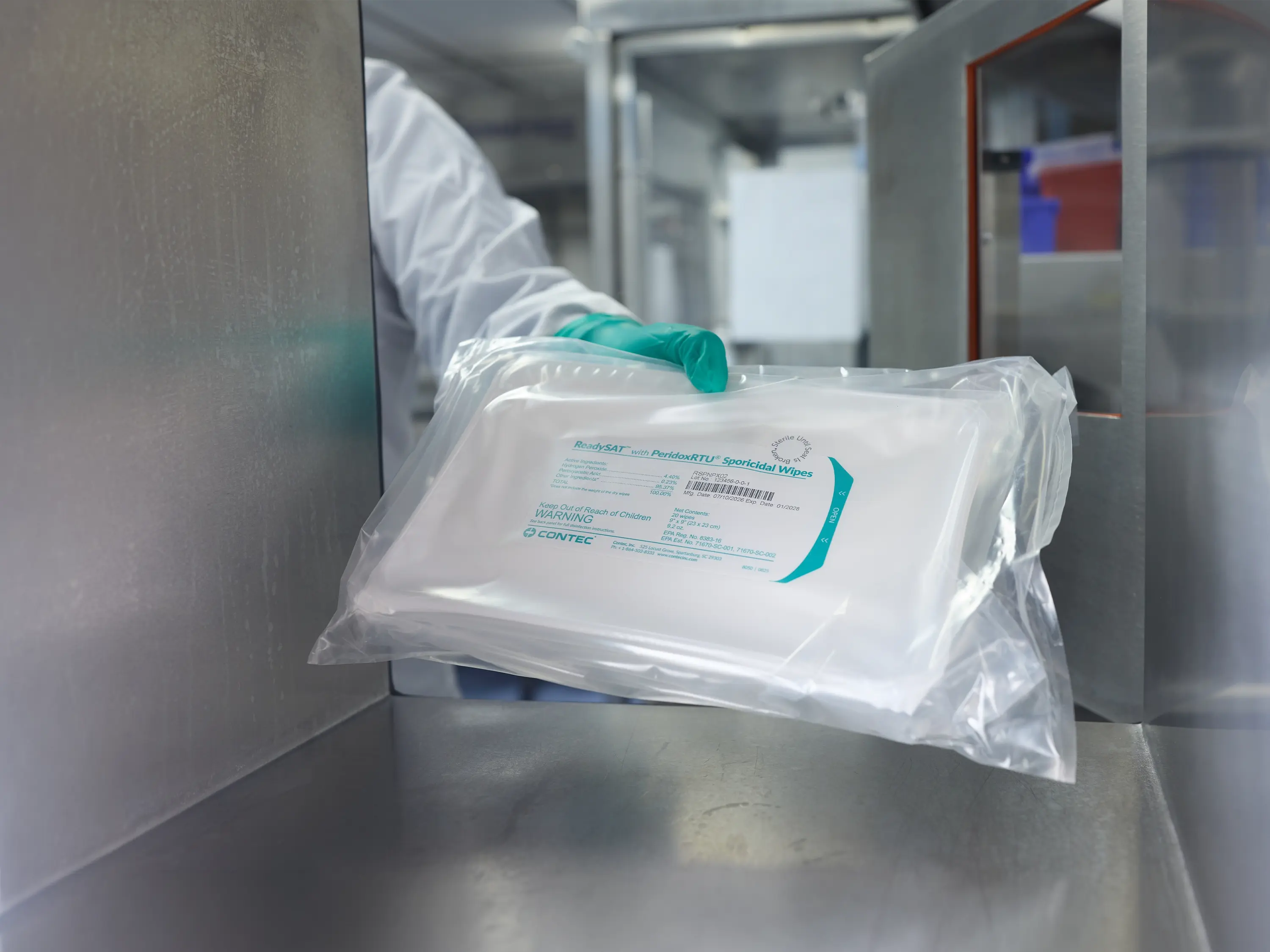 Gloved cleanroom operator transferring a sealed package of ReadySAT with PeridoxRTU Sporicidal Wipes through a cleanroom passthrough.