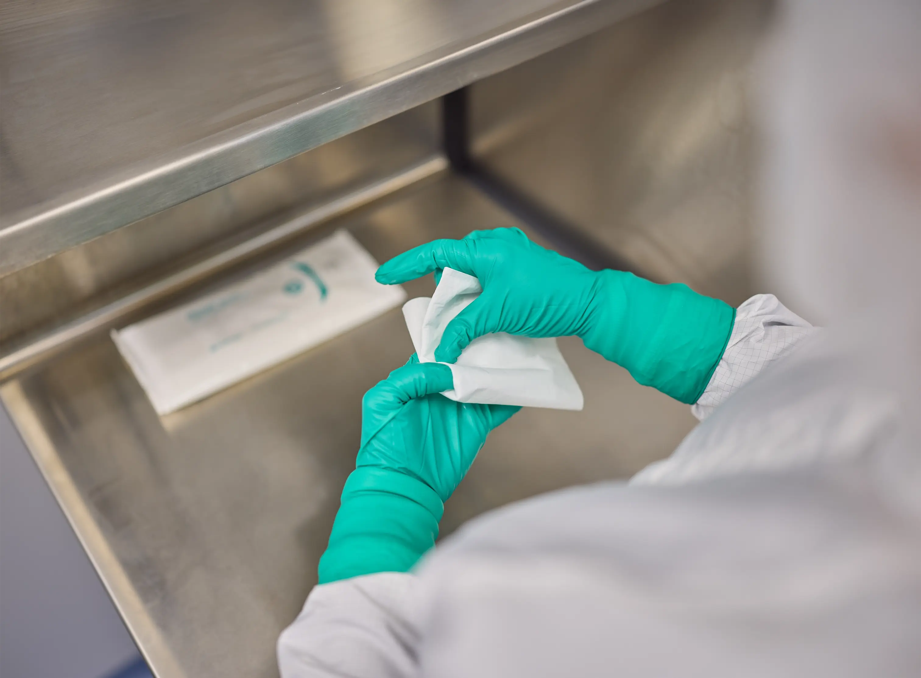 Operator in a life sciences cleanroom environment folding a presaturated wipe to prepare for wiping a surface.